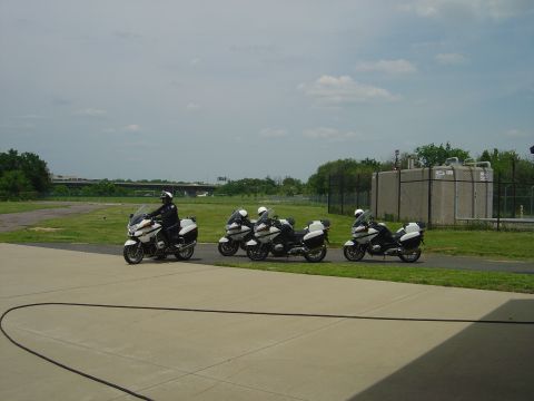 2001 Ford Crown Victoria - Four police motorcycles are lined up on a paved area with a grassy field and industrial buildings in the background.