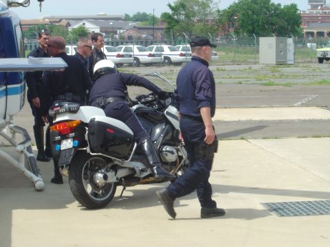 2001 Ford Crown Victoria - Law enforcement personnel are seen with a motorcycle and helicopter, with parked vehicles in the distance.