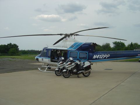 2001 Ford Crown Victoria - A helicopter and two police motorcycles are parked on an airfield under a cloudy sky.
