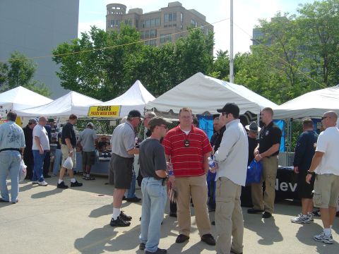 2001 Ford Crown Victoria - An outdoor event is underway with several tents set up and many people milling about. A sign advertising "CIGARS POLICE WEEK COINS" is visi…