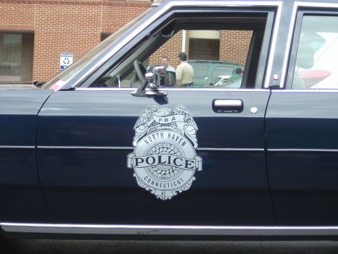 2001 Ford Crown Victoria - Side view of a police car door showing the North Haven Police badge; two men are inside.