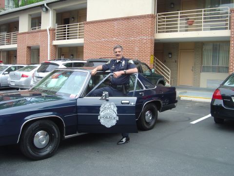 2001 Ford Crown Victoria - A police officer stands next to a parked police car outside a motel.