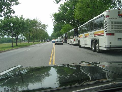 2001 Ford Crown Victoria - A procession of charter buses and cars are lined up on a road, viewed from the perspective of a driver.