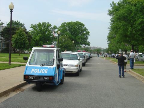 2001 Ford Crown Victoria - Several police vehicles are parked in a row on a street, with a three-wheeled patrol vehicle in the foreground.