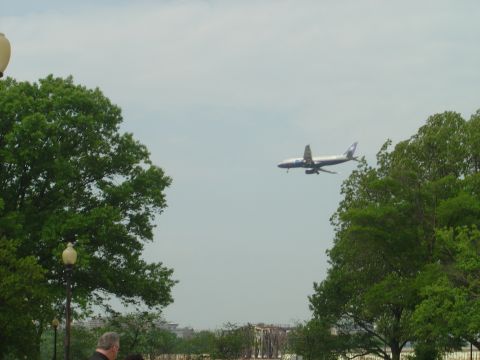 2001 Ford Crown Victoria - An airplane flies through a hazy sky, framed by lush green trees and distant urban structures.