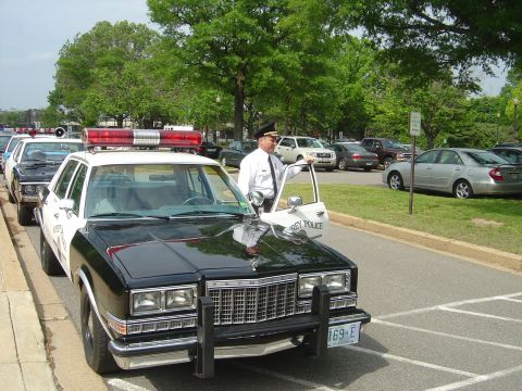 2001 Ford Crown Victoria - A police officer stands by a black and white police car parked in a lot.