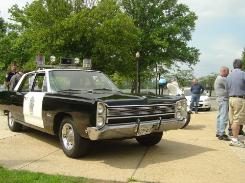 2001 Ford Crown Victoria - This vintage police car, a Plymouth, is on display with onlookers nearby.