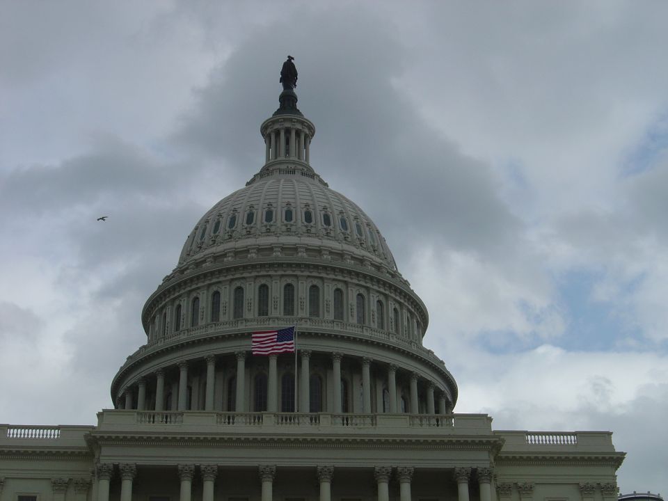 US Capitol Building dome with American flag and cloudy sky