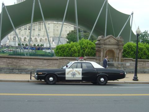 2001 Ford Crown Victoria - A 1977 Dodge Monaco, marked as Highway Patrol, is parked in front of a building with a large green canopy.