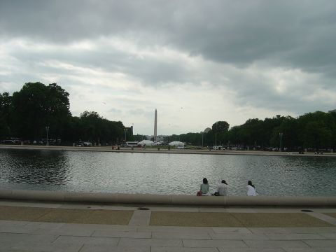 2001 Ford Crown Victoria - A view of the Washington Monument and Reflecting Pool on a cloudy day, with several people relaxing by the water's edge.