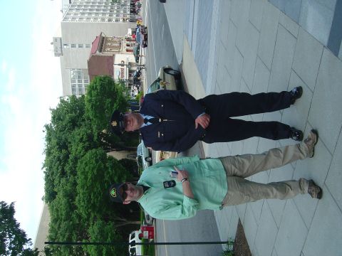 2001 Ford Crown Victoria - Two men stand on a sidewalk in front of a police car and buildings.