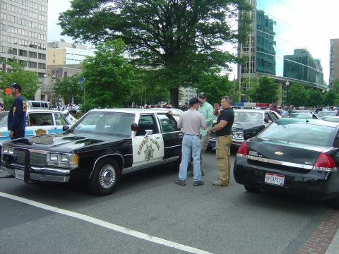 2001 Ford Crown Victoria - Several police vehicles are parked on a city street, with people gathered around one of them.