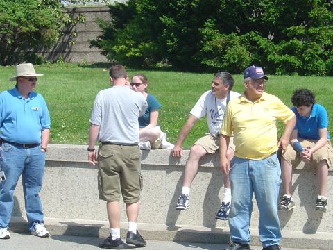 2001 Ford Crown Victoria - People gather outdoors on a bright day, with some seated on a low wall and others standing nearby.
