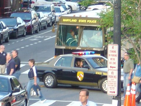 2001 Ford Crown Victoria - A Maryland State Police car with lights on is parked next to a bus, with pedestrians crossing the street.