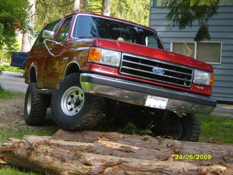 1989 Ford Bronco - This lifted Ford Bronco is shown with its front tires on top of a large fallen tree.