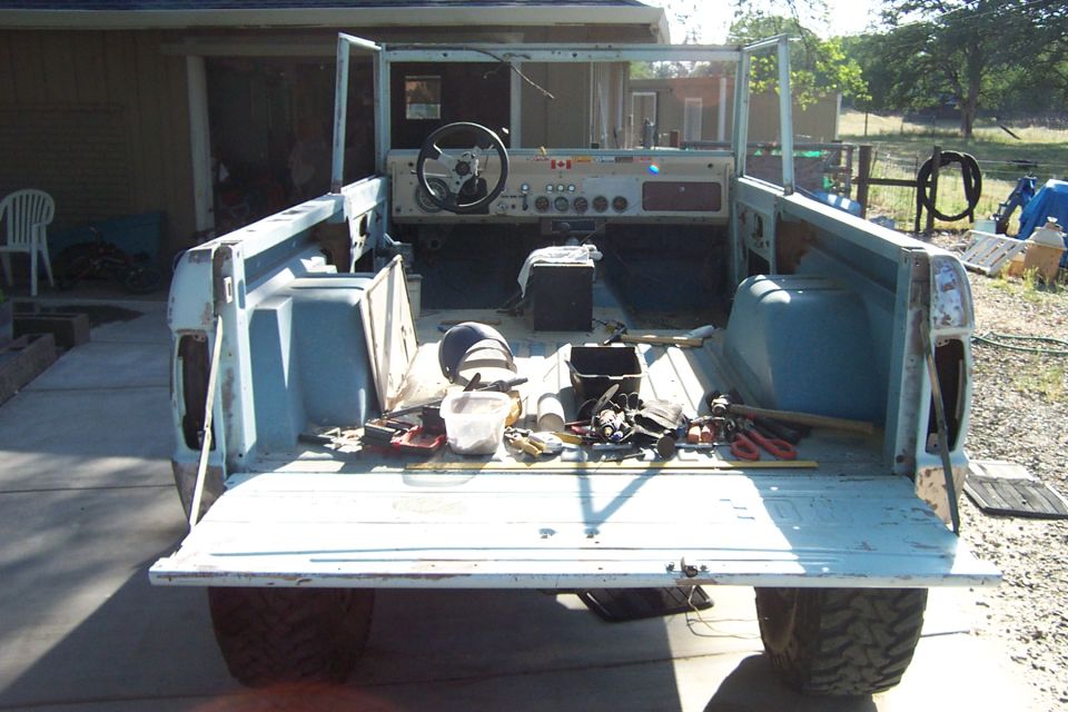 Back view of a light blue Ford Bronco with the tailgate down, showing the interior and tools scattered in the bed