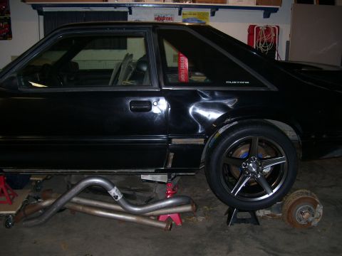 1990 Ford Mustang - A black 1990 Ford Mustang coupe is shown on jack stands with its exhaust system laid out nearby.