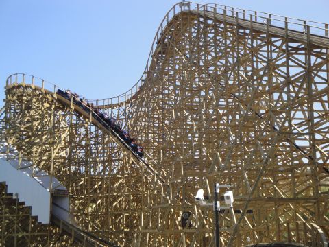 1993 Ford Taurus - A roller coaster train ascends a wooden track under a clear blue sky.