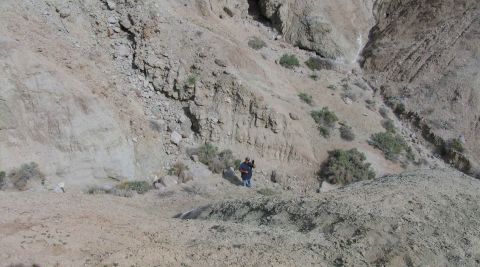 1984 Ford Bronco - A lone figure stands on a barren, arid slope, dwarfed by the surrounding geological formations.
