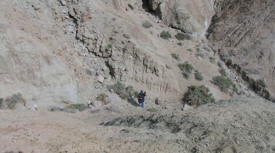 Person standing on a dusty, rocky hillside with sparse vegetation