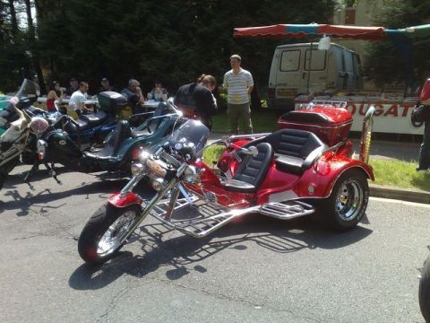 1991 Ford Crown Victoria - A red trike motorcycle is parked outdoors with other vehicles and people in the background.