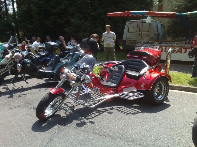 Red trike motorcycle with two seats and chrome accents parked next to other motorcycles