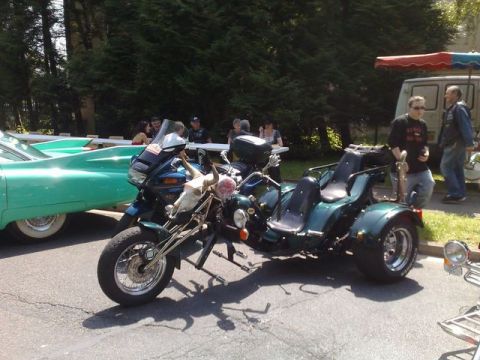 1991 Ford Crown Victoria - A custom trike a bull skull is displayed at an outdoor event, with a classic teal car visible to its left.