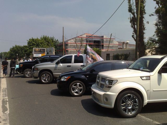 Several vehicles parked on a street, including a white SUV, a black car, a silver pickup truck, and a black pickup truck. Construction is visible in the background
