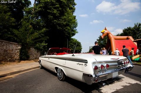 1991 Ford Crown Victoria - A white 1961 Chevrolet Impala convertible is parked on a street, with an inflatable horse in the background.