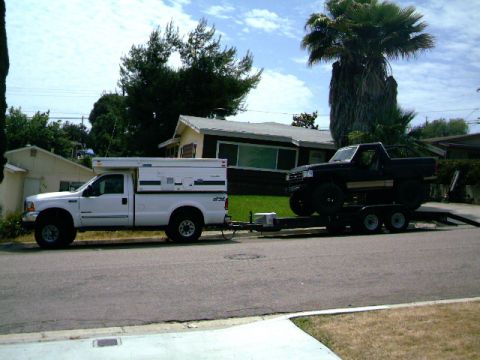 2000 Ford F-250 - White Ford F-250 with camper shell is seen towing a black Ford Bronco on a trailer.