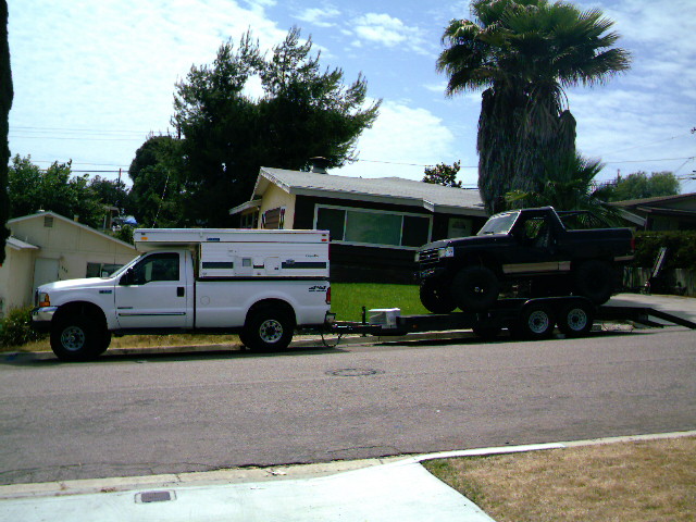 White Ford Super Duty truck with camper towing trailer carrying a Bronco