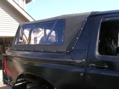 1996 Ford Bronco - The rear section of a black Ford Bronco, fitted with a soft top and roll cage, is shown from the side.