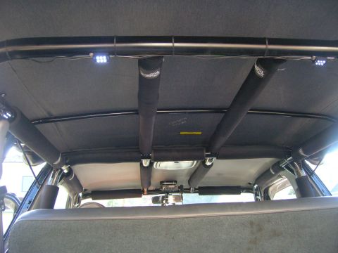 1996 Ford Bronco - The interior of a vehicle shows a custom roll cage structure with added LED lighting and padded support bars.