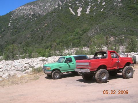 1985 Ford Bronco - Two Ford Broncos, one green and one red, are parked in a scenic, rocky outdoor location.