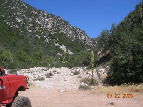 1985 Ford Bronco - Red off-road vehicle parked on a dirt road in a mountainous area with dry vegetation.