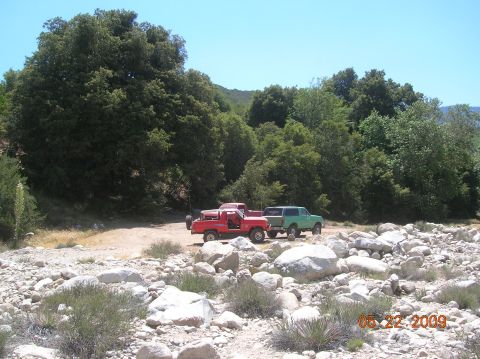 1985 Ford Bronco - Two trucks are parked in a rocky, wooded area on a sunny day.
