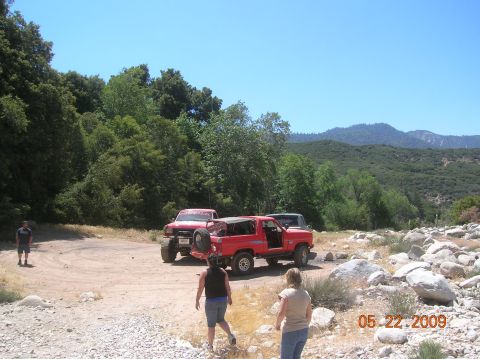1985 Ford Bronco - Several off-road vehicles are parked in a rocky, wooded area on a sunny day.