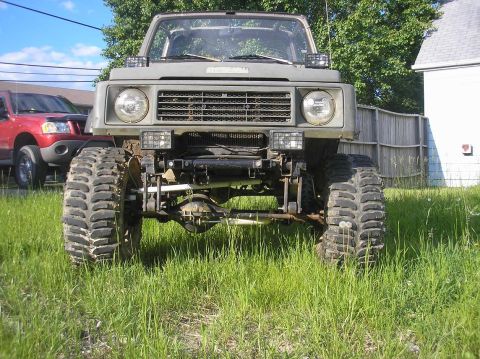 1987 Suzuki Samurai - This heavily modified vehicle has oversized tires and a lifted suspension, parked in a grassy yard.