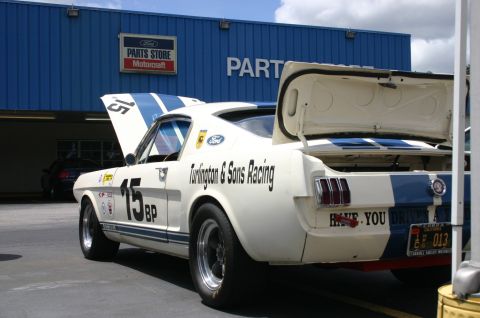 1968 Shelby GT500 - A white 1967 Ford Mustang race car with blue stripes and racing decals is parked in front of a Ford Parts Store.