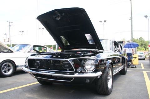 1968 Shelby GT500 - A black 1968 Shelby GT500 is displayed with its hood open at a car show, alongside another classic Mustang.