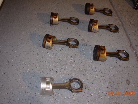 1995 Ford Taurus - Several engine pistons and connecting rods are laid out on a garage floor.