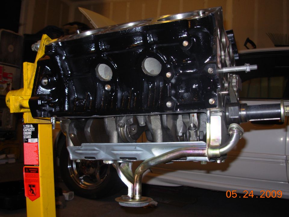 Black engine block on yellow engine stand, with oil pan and pickup tube attached. Date stamp 05.24.2009