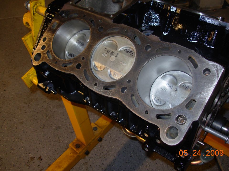 Engine block with three pistons visible, labeled Cyl #1, Cyl #2, and Cyl #3. The block is black and mounted on a yellow engine stand