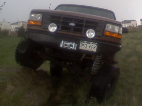 1993 Ford Bronco - A lifted 1992 Ford Bronco is angled on uneven terrain, showing its front grille and off-road modifications.