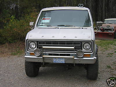 1978 Ford E250 - A silver Ford van with a chrome grille guard and auxiliary lights is parked outdoors, with another vehicle visible in the background.