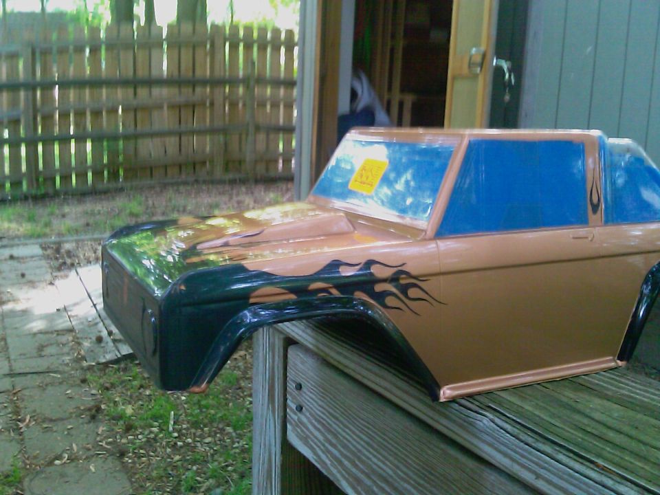 Tan and green Ford Bronco body shell with flame decals, resting on wooden planks