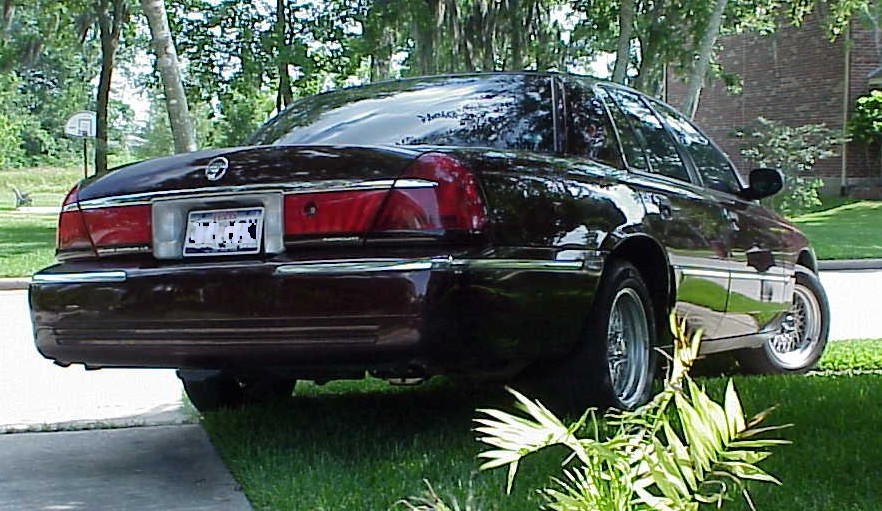 Maroon Mercury Grand Marquis sedan, rear-quarter view parked on grass by trees