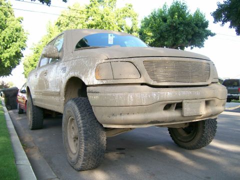 1995 Ford Bronco - This lifted pickup truck is covered in mud, suggesting recent off-road use.