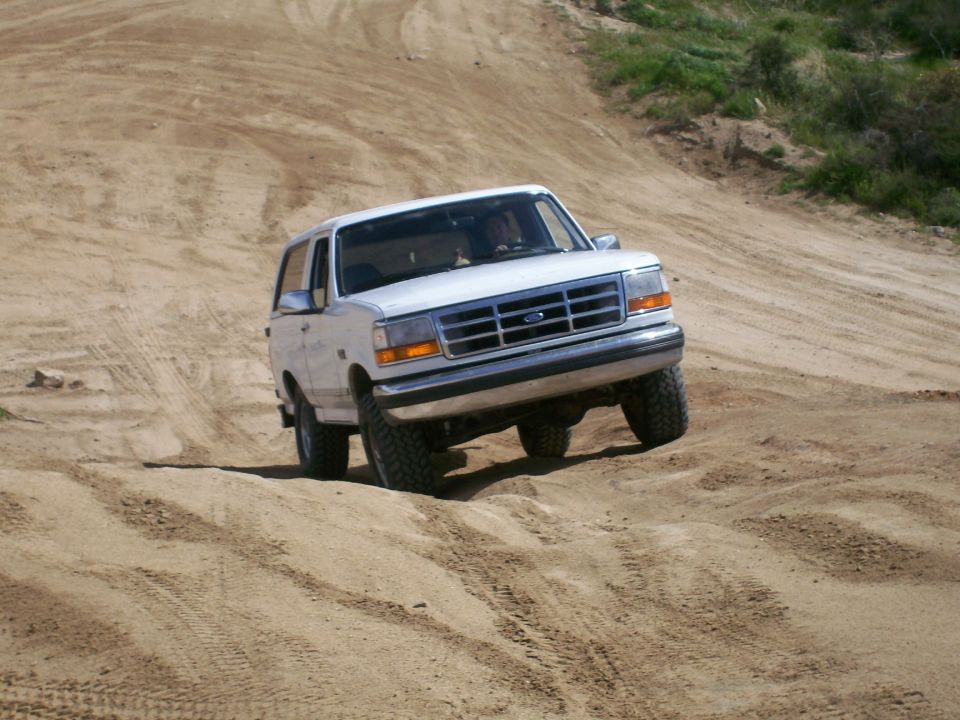 White lifted Ford Bronco SUV driving over a sandy dirt mound, front view
