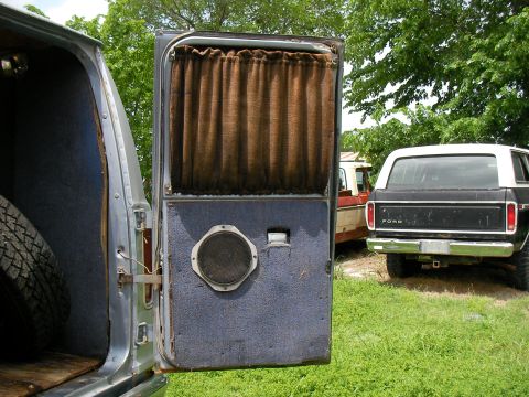 1978 Ford E250 - The interior of a van door is open, revealing a speaker and brown curtain, with the rear of a black Ford SUV in the background.